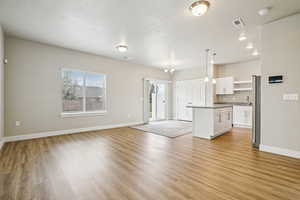 Unfurnished living room featuring a chandelier, light wood-type flooring, and a textured ceiling