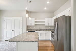 Kitchen with stainless steel appliances, light stone counters, decorative light fixtures, a kitchen island, and white cabinets