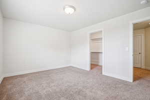 Unfurnished bedroom with light carpet and a walk in closet