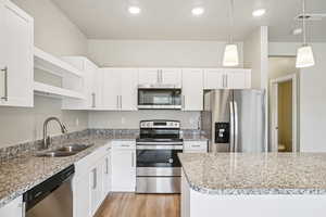 Kitchen with stainless steel appliances, white cabinetry, open shelves, and light stone countertops