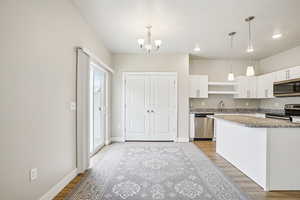 Kitchen featuring white cabinets, stainless steel appliances, light wood finished floors, light stone countertops, and a chandelier