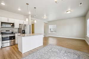 Kitchen with stainless steel appliances, white cabinets, light wood-style flooring, open floor plan, and light stone counters