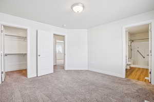 Unfurnished bedroom featuring light colored carpet, a walk in closet, and connected bathroom