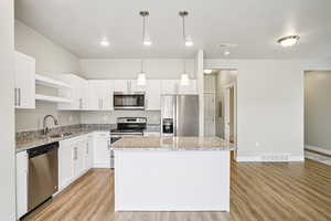 Kitchen featuring stainless steel appliances, light wood finished floors, and light stone counters