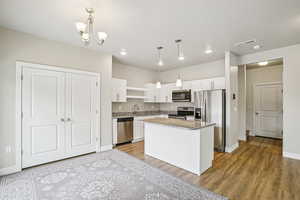 Kitchen featuring stainless steel appliances, white cabinets, light stone countertops, a kitchen island, and light wood-type flooring