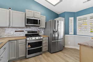 Kitchen featuring wood counters, stainless steel appliances, gray cabinetry, light wood-type flooring, and tasteful backsplash