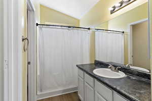 Full bathroom with vanity, light wood-style floors, lofted ceiling, and a shower with curtain