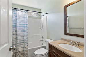 Bathroom with a textured wall, vanity, and shower / bath combination with curtain