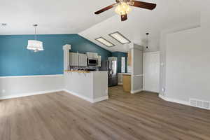 Kitchen featuring a peninsula, stainless steel appliances, a ceiling fan, and light wood finished floors