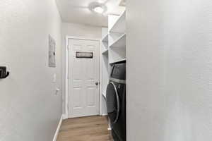 Laundry area with a textured wall, light wood-style flooring, washer / dryer, and electric panel