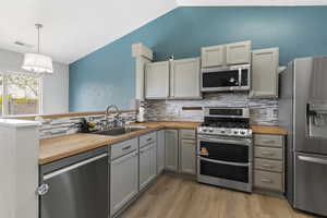 Kitchen featuring butcher block counters, stainless steel appliances, vaulted ceiling, a peninsula, and light wood-type flooring