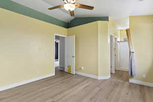 Unfurnished bedroom featuring ceiling fan, lofted ceiling, light wood-style flooring, and ensuite bath