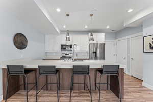Two tone kitchen with a peninsula, a breakfast bar area, light wood-type flooring, stainless steel appliances, and two tone cabinets
