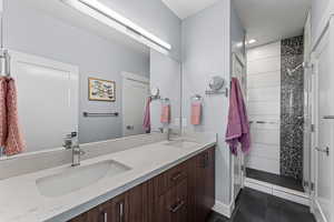 Bathroom featuring a stall shower, double vanity, and dark tile patterned flooring
