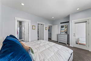 Bedroom with dark carpet, a spacious closet, ensuite bathroom, access to outside, and recessed lighting