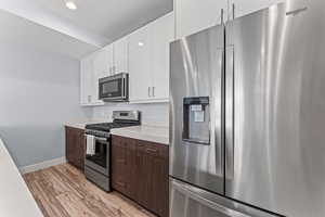 Dual tone kitchen featuring stainless steel appliances, dual tone cabinetry, light wood finished floors, and recessed lighting