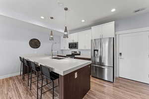 Dual tone kitchen with a peninsula, a kitchen bar, stainless steel appliances, dual tone cabinets, and light wood-type flooring