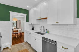 Kitchen featuring white cabinets, stainless steel dishwasher, light stone counters, light tile patterned floors, and decorative light fixtures