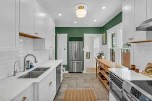 Kitchen featuring stone tile floors, stainless steel appliances, tasteful backsplash, white cabinets, and recessed lighting
