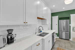 Kitchen with stainless steel appliances, backsplash, white cabinetry, light stone countertops, and light stone finish floors