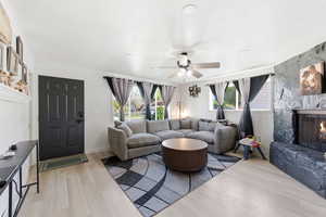 Living area with healthy amount of natural light, ceiling fan, a fireplace, and light wood-type flooring