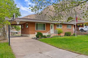 View of front facade with a carport, a front lawn, brick siding, and driveway