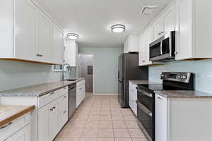Kitchen featuring stainless steel appliances, white cabinetry, a textured ceiling, light stone counters, and light tile patterned floors