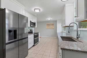 Kitchen featuring stainless steel appliances, light stone counters, white cabinetry, a textured ceiling, and light tile patterned floors