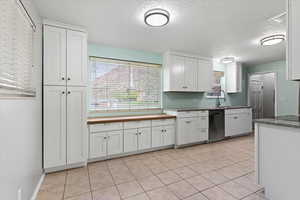 Kitchen featuring white cabinets, dishwasher, a textured ceiling, light tile patterned floors, and butcher block countertops