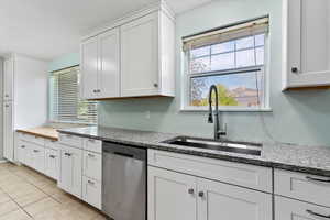 Kitchen with white cabinetry, dishwasher, light stone counters, light tile patterned floors, and a textured ceiling