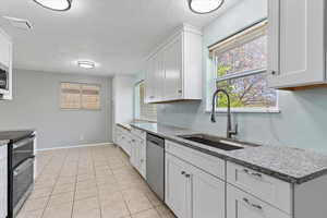 Kitchen featuring white cabinets, stainless steel appliances, a textured ceiling, light stone countertops, and light tile patterned flooring