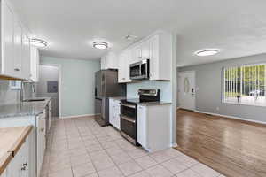 Kitchen with light tile patterned flooring, white cabinetry, stainless steel appliances, light stone countertops, and a textured ceiling