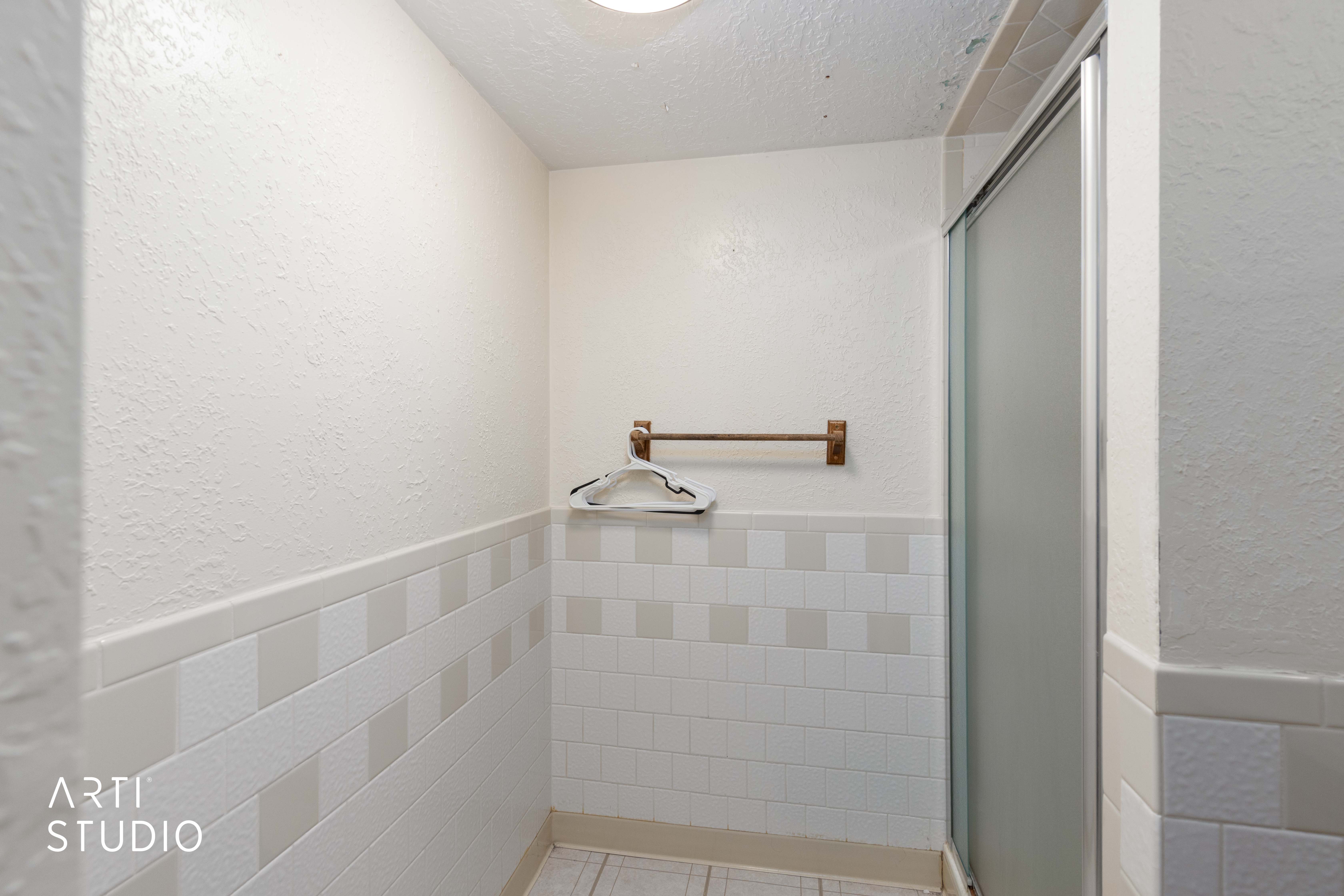 Full bath with a wainscoted wall, a textured ceiling, a textured wall, tile walls, and a shower stall