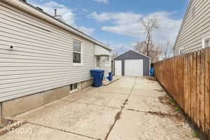 View of patio with concrete driveway, a detached garage, and an outbuilding