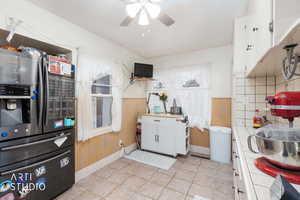 Kitchen featuring stainless steel refrigerator with ice dispenser, white cabinetry, wainscoting, a ceiling fan, and tile countertops