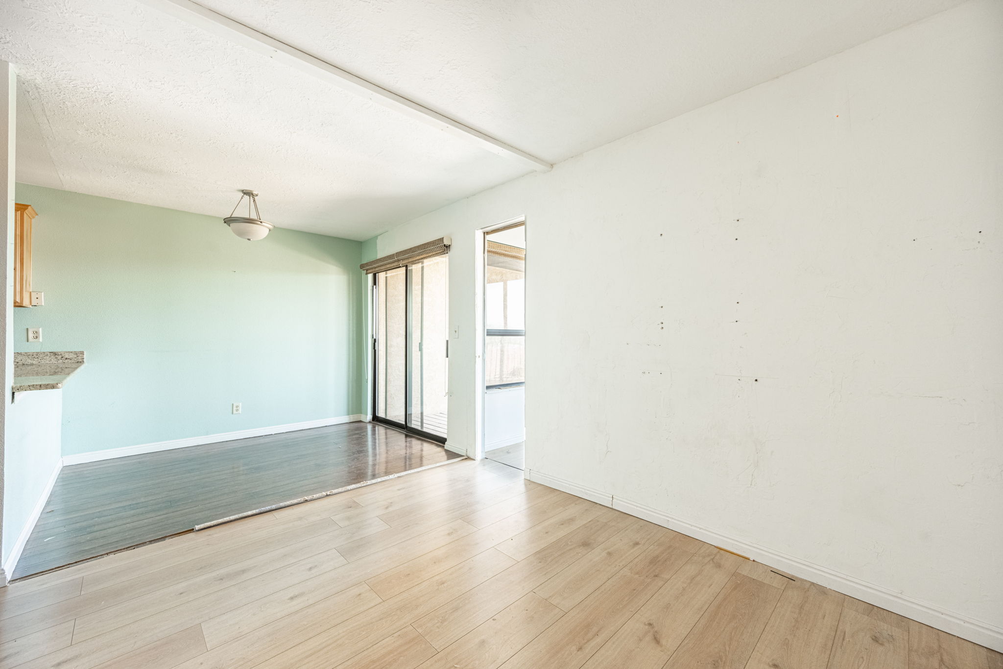 Open concept living area featuring light wood-finish flooring, a wall with light blue paint, and a sliding glass door