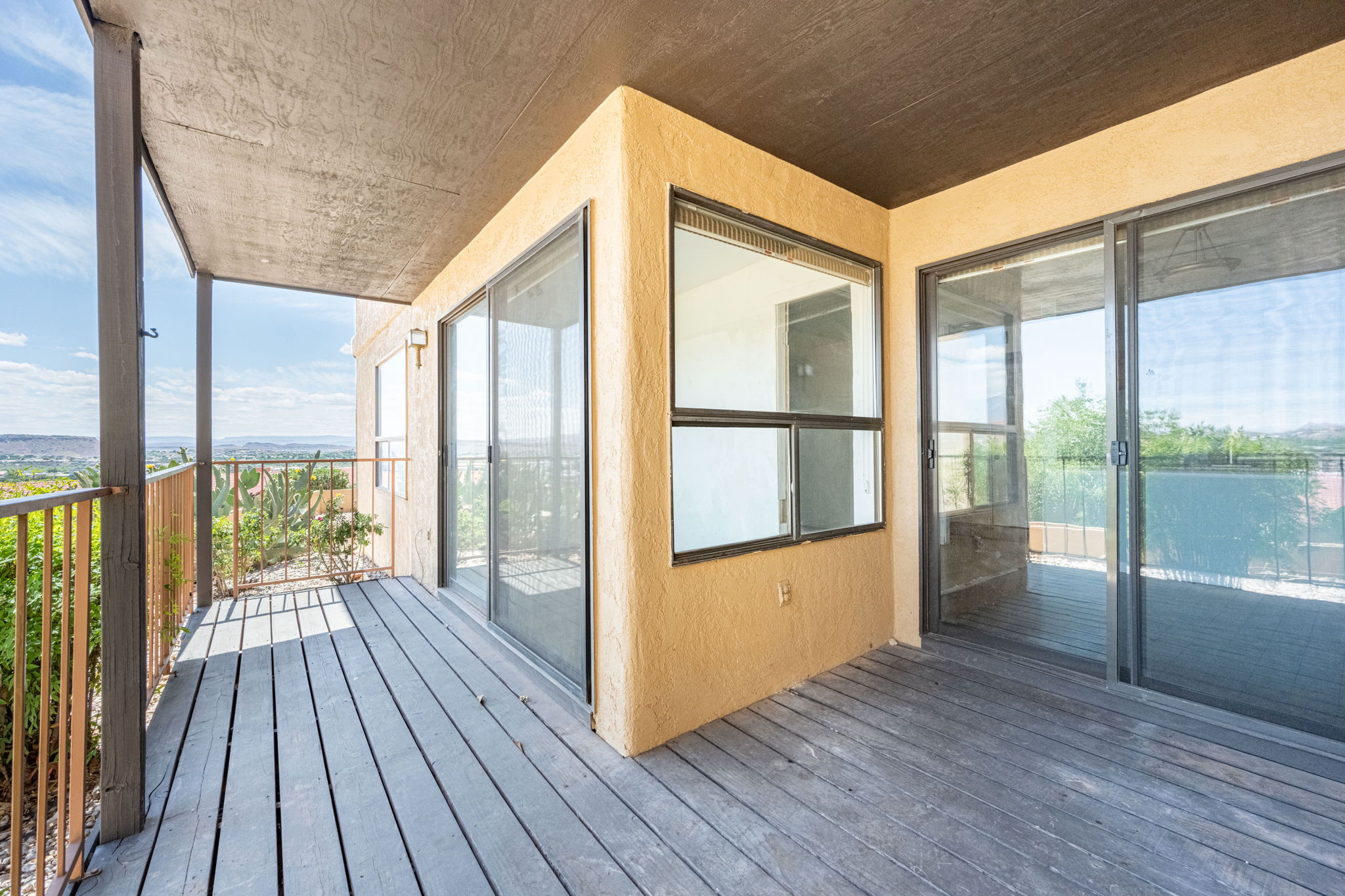 Covered outdoor deck with plank flooring, featuring multiple sliding glass doors and an additional window