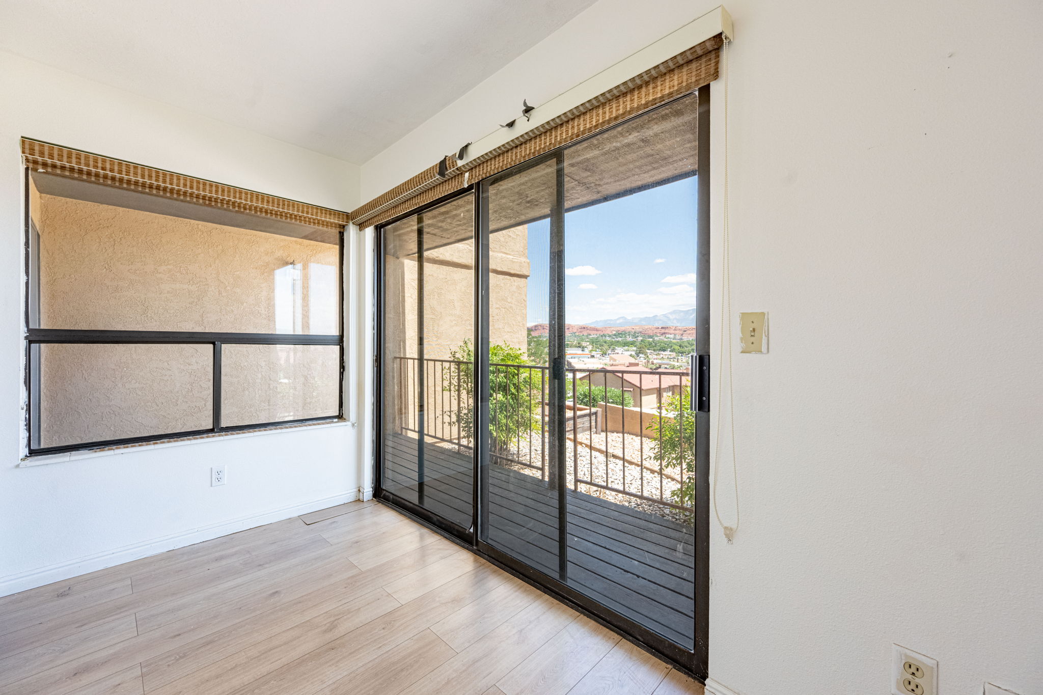 Room featuring wood-finish flooring, a large window, and sliding glass doors opening to a balcony with metal railings
