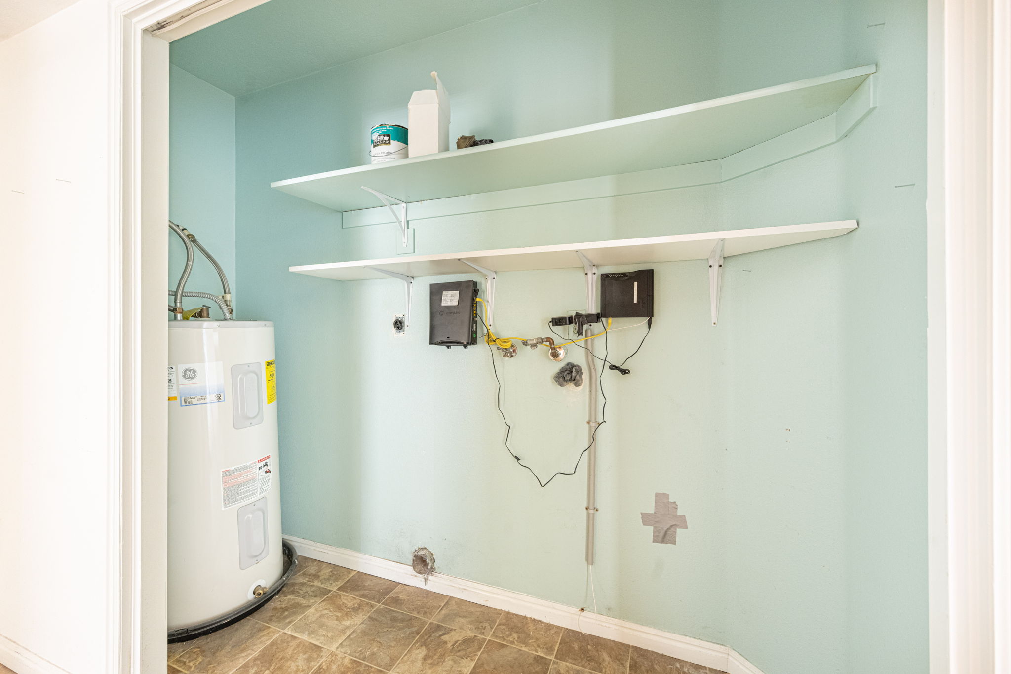 Utility closet featuring a water heater, two wall-mounted storage shelves, and durable vinyl flooring