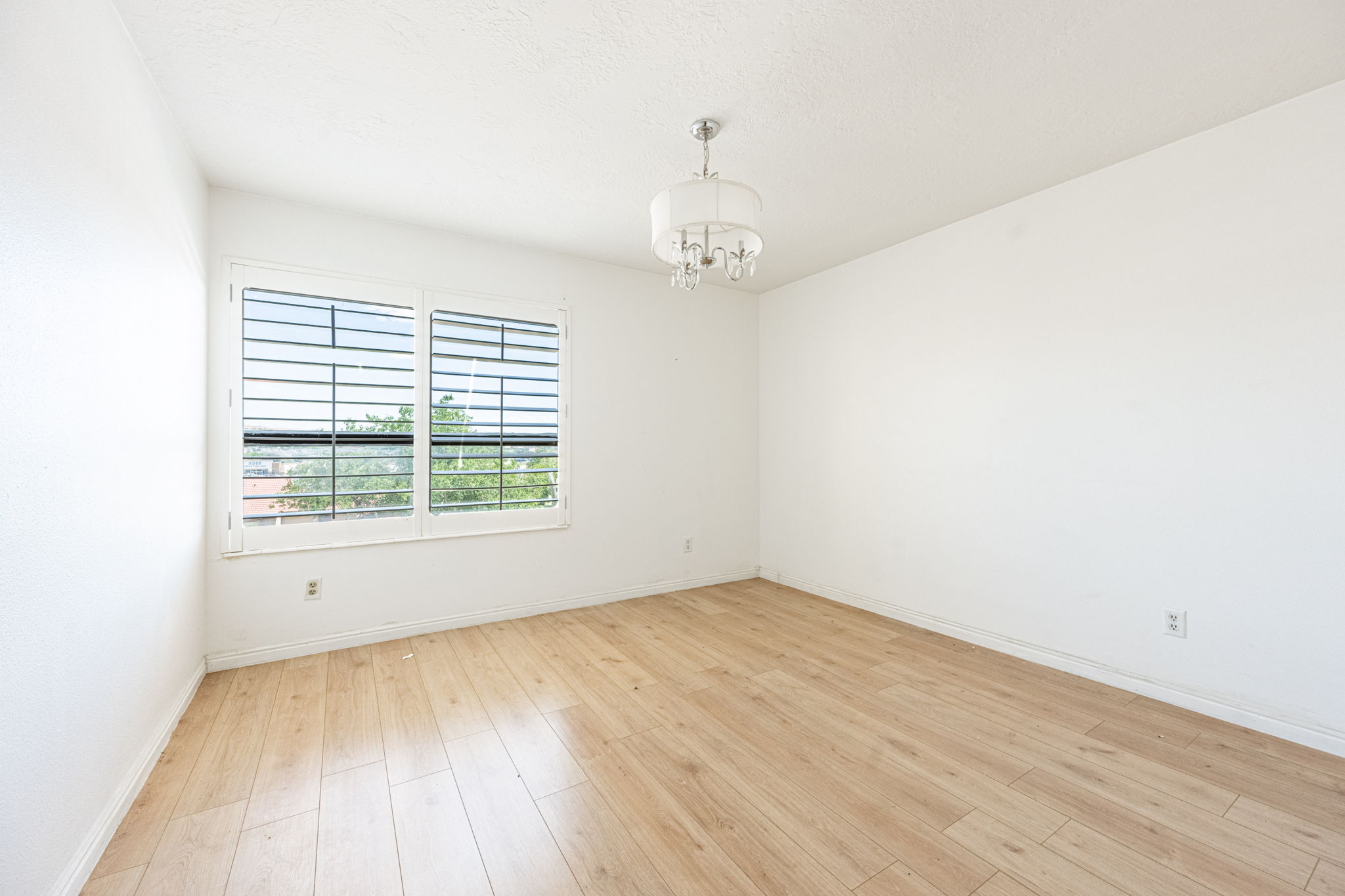 Room with wood-finish flooring, white walls, and a multi-pane window with horizontal blinds