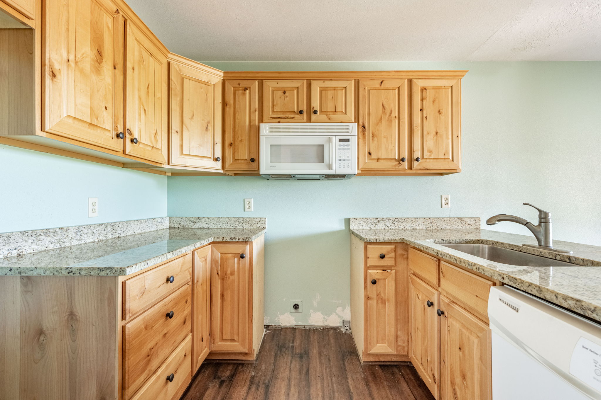 Kitchen featuring wood cabinetry, light-toned countertops, an undermount sink with a gooseneck faucet, a built-in microwave, and wood-finish flooring