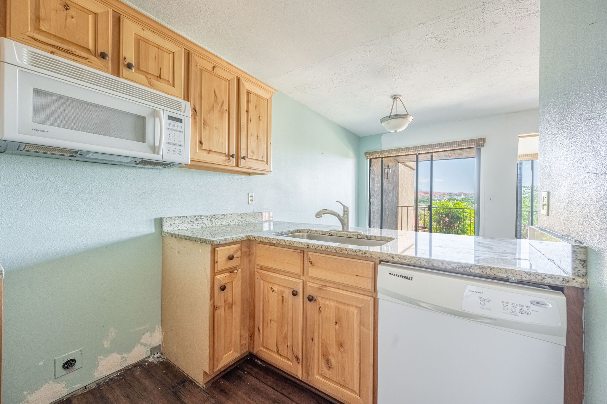 Kitchen featuring wood-finish cabinetry, light-toned granite-style countertops, an undermount sink with a chrome faucet, a built-in microwave, and a white dishwasher