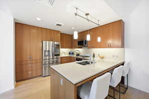 Kitchen featuring wood finish cabinets, a breakfast bar, stainless steel appliances, a peninsula, and light wood-type flooring