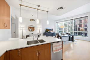 Kitchen featuring open floor plan, wood finish cabinetry, stainless steel dishwasher, decorative light fixtures, and a peninsula