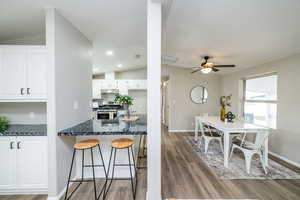 Kitchen with stainless steel gas range, a kitchen breakfast bar, vaulted ceiling, white cabinets, and light wood-style floors