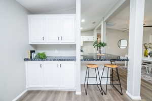 Kitchen with white cabinetry, dark stone countertops, light wood finished floors, vaulted ceiling, and ceiling fan