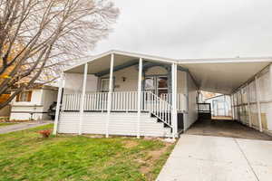 Manufactured / mobile home featuring a porch, a storage shed, a carport, driveway, and a front lawn
