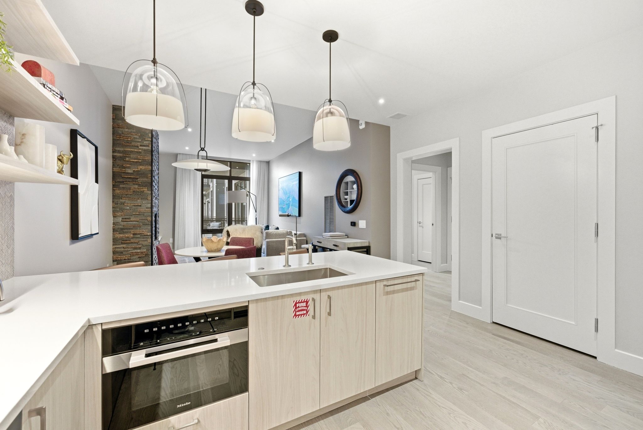 Kitchen with stainless steel oven, a peninsula, open shelves, pendant lighting, and light stone counters