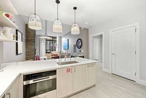 Kitchen with stainless steel oven, a peninsula, open shelves, pendant lighting, and light stone counters