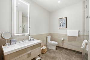 Bathroom featuring vanity, a tile shower, tile walls, and wainscoting